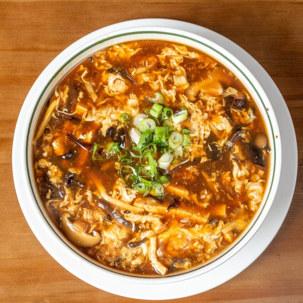 Hot and sour soup with egg, mushrooms, tofu, and scallions in a white bowl on wood.