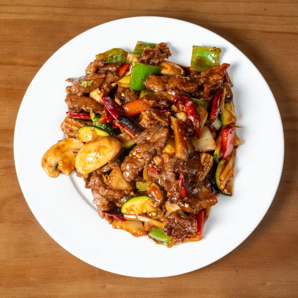 Spicy beef stir-fry with green peppers, mushrooms, zucchini, and red chilies on a white plate.