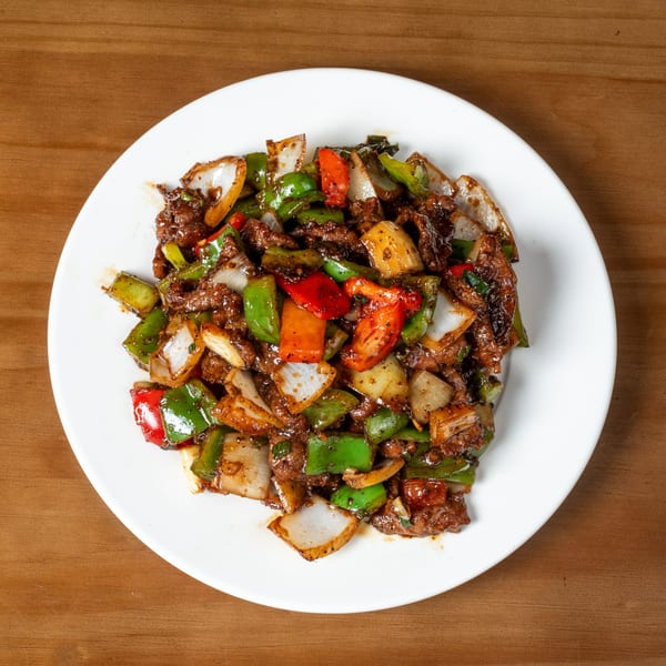 Black pepper beef stir-fry with green and red bell peppers and onions on a white plate.