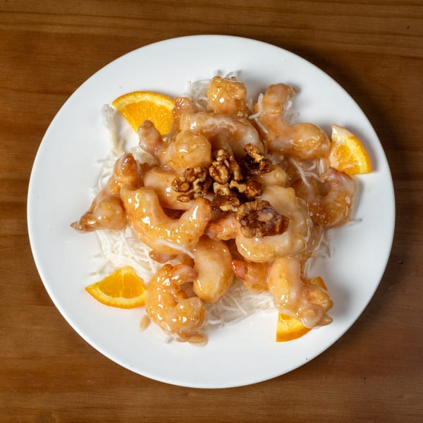 Honey walnut shrimp with orange slices and shredded daikon radish on a white plate.