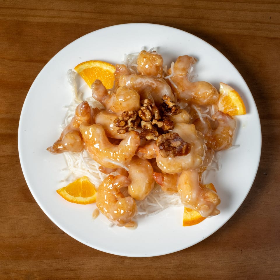 Honey walnut shrimp with orange slices and shredded daikon radish on a white plate.