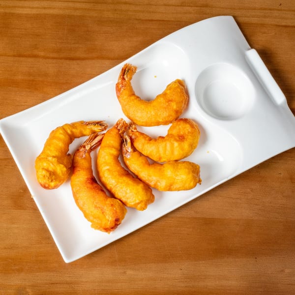 Golden-brown fried shrimp arranged on a white rectangular serving dish with sauce wells.