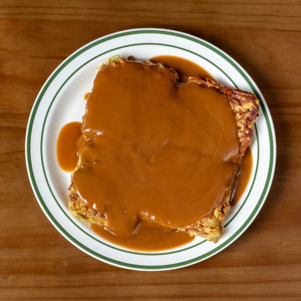A square-shaped omelet covered in brown gravy, served on a white plate with green stripes.