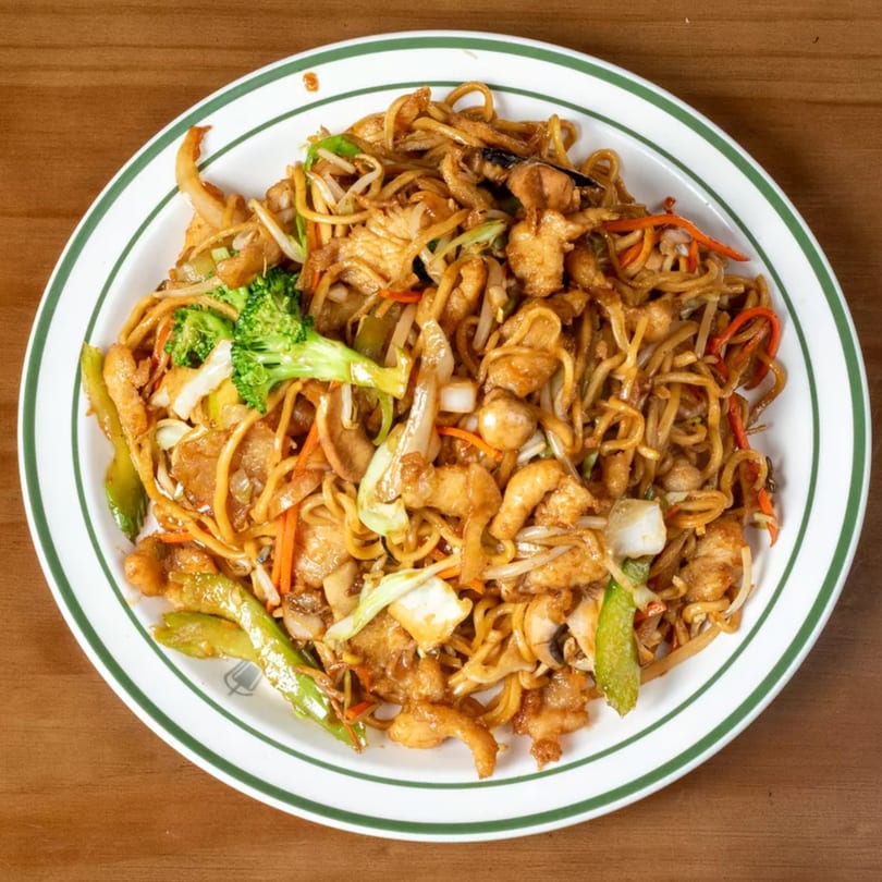 A white plate with green stripes holds a large serving of chicken lo mein with vegetables.