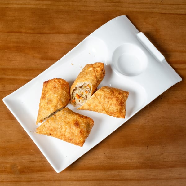 Four golden-brown egg rolls, one cut open to show the filling, on a white rectangular plate with a sauce well.