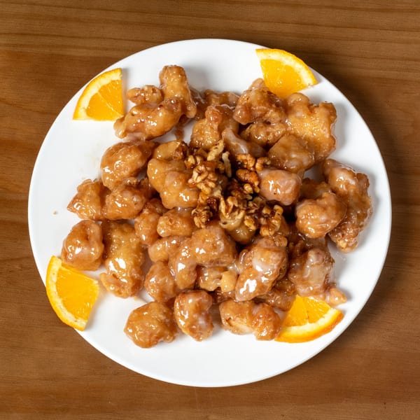 Honey walnut shrimp with orange slices on a white plate.
