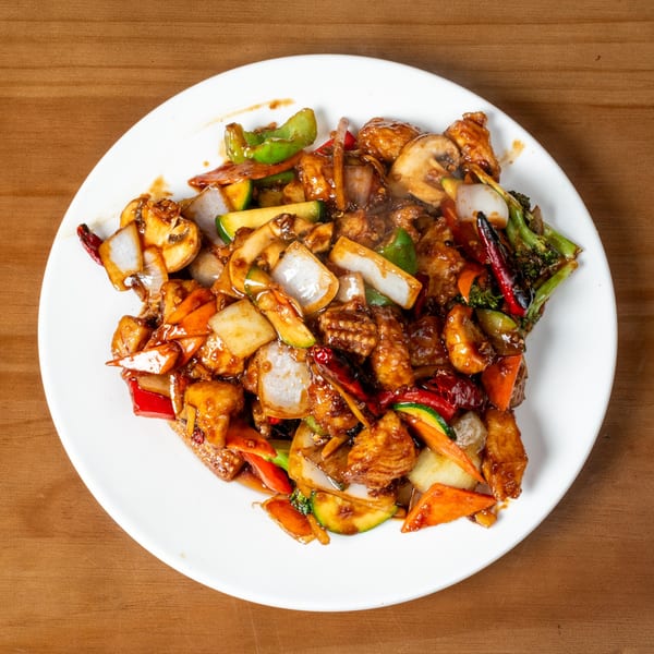 Stir-fried chicken with mixed vegetables, including onions, bell peppers, zucchini, and mushrooms, on a white plate.