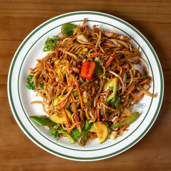 Close-up of a plate of lo mein noodles with mixed vegetables like broccoli, carrots, and zucchini.