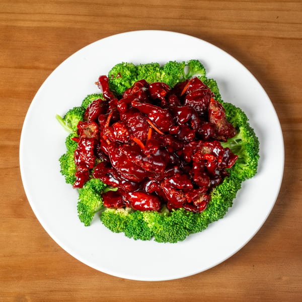 Sweet and sour chicken with red sauce and broccoli florets on a white plate.